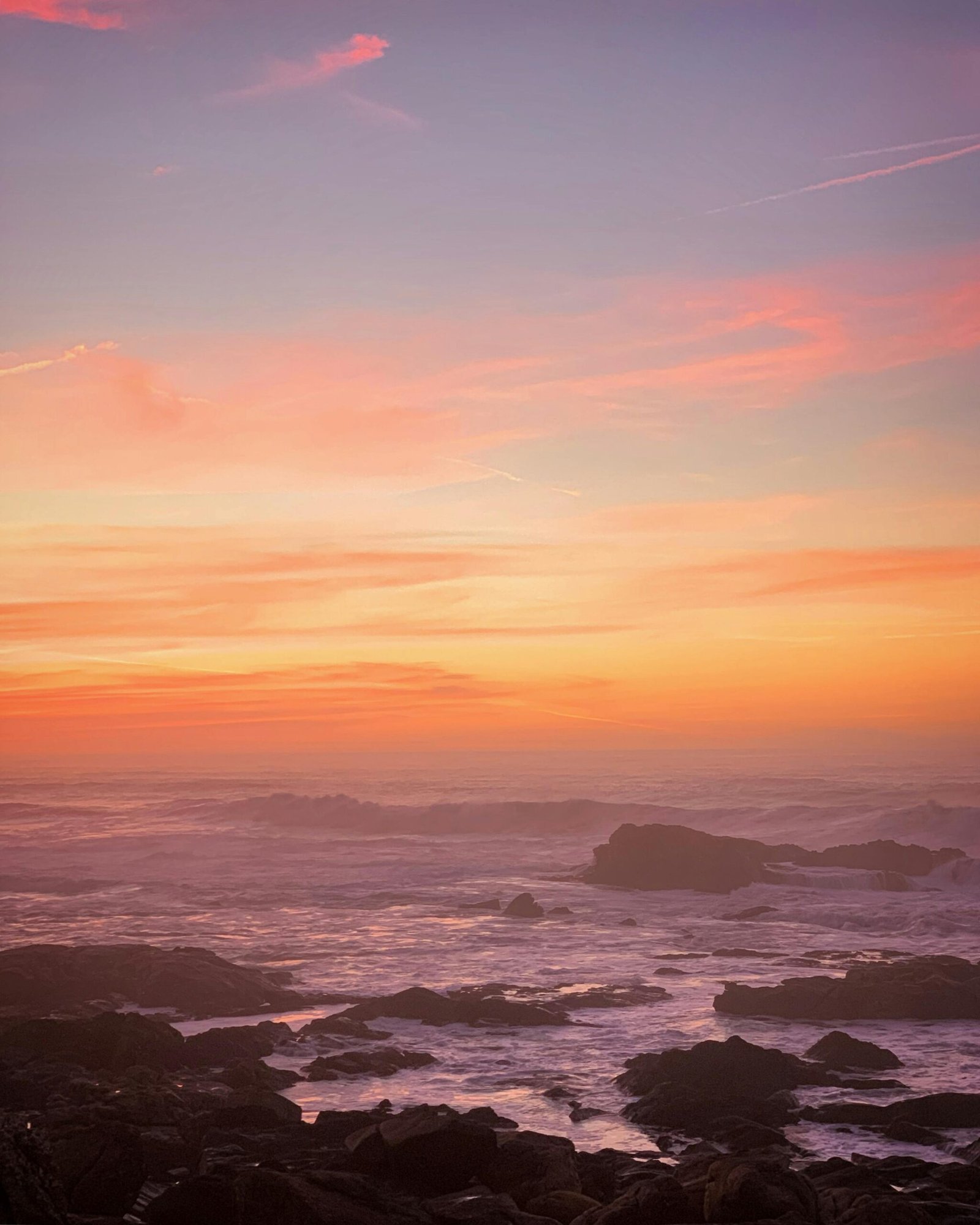 Beautiful sunset view over rocky coast with vibrant sky and calm Atlantic Ocean waves.
